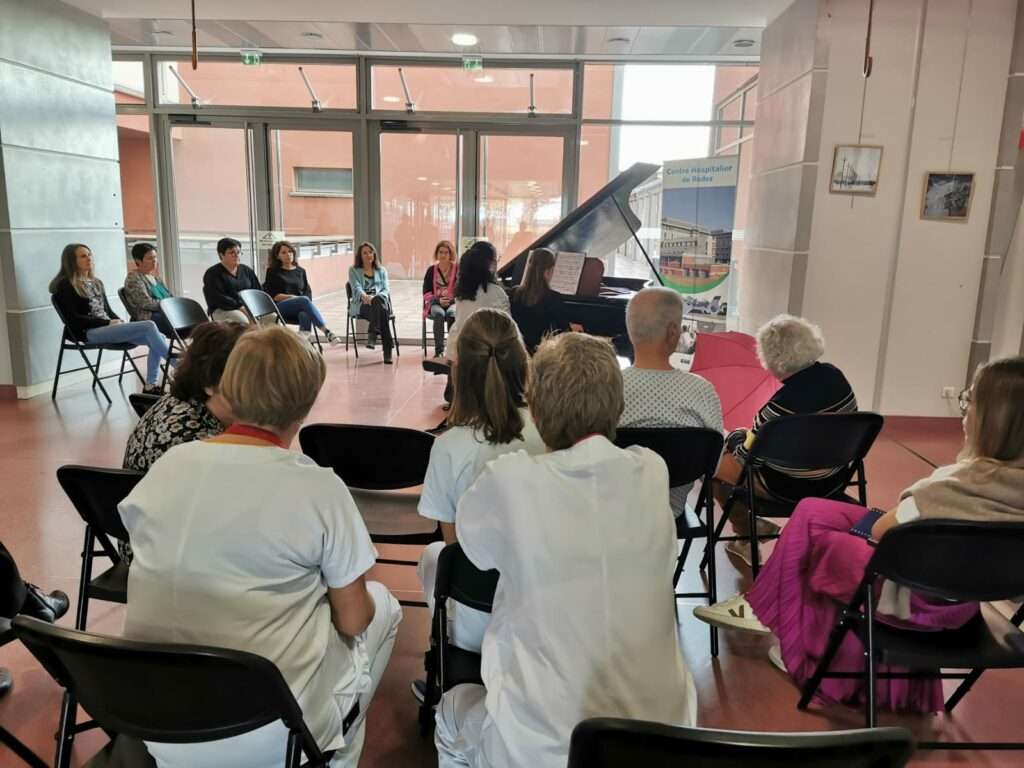 Patients, professionnels et visiteurs assis autour du piano 