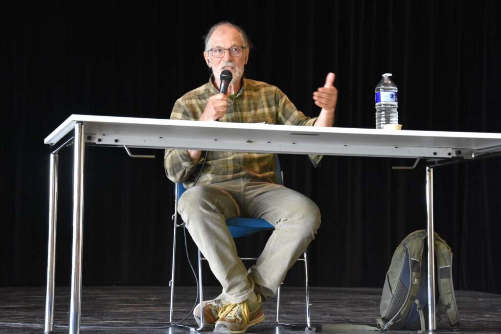 David LE BRETON pendant sa conférence, assis à une table, le micro à la main 